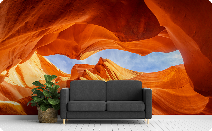 Orange canyon wallpaper mural with curved rock formations and a blue sky opening behind a dark gray sofa